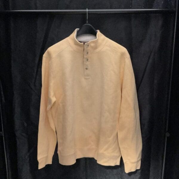 A tan colored shirt hanging on a black wall.