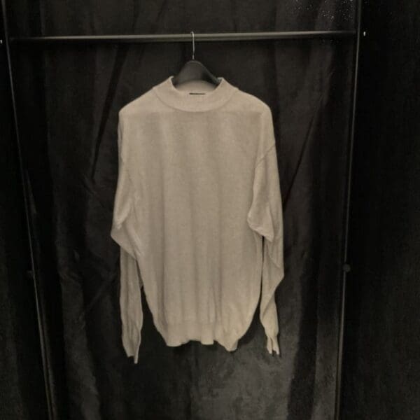 A white sweater hanging on a black curtain.