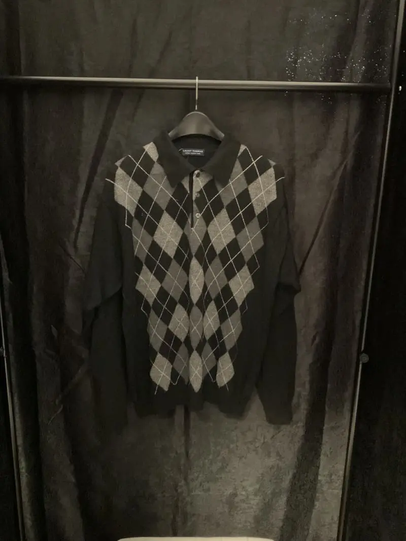 A black and white argyle sweater hanging on a rack.