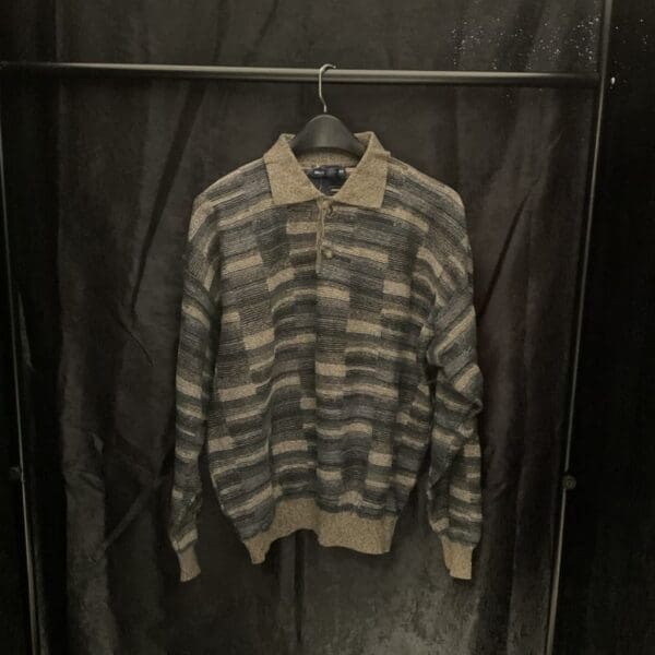 A sweater hanging on the wall in front of a curtain.