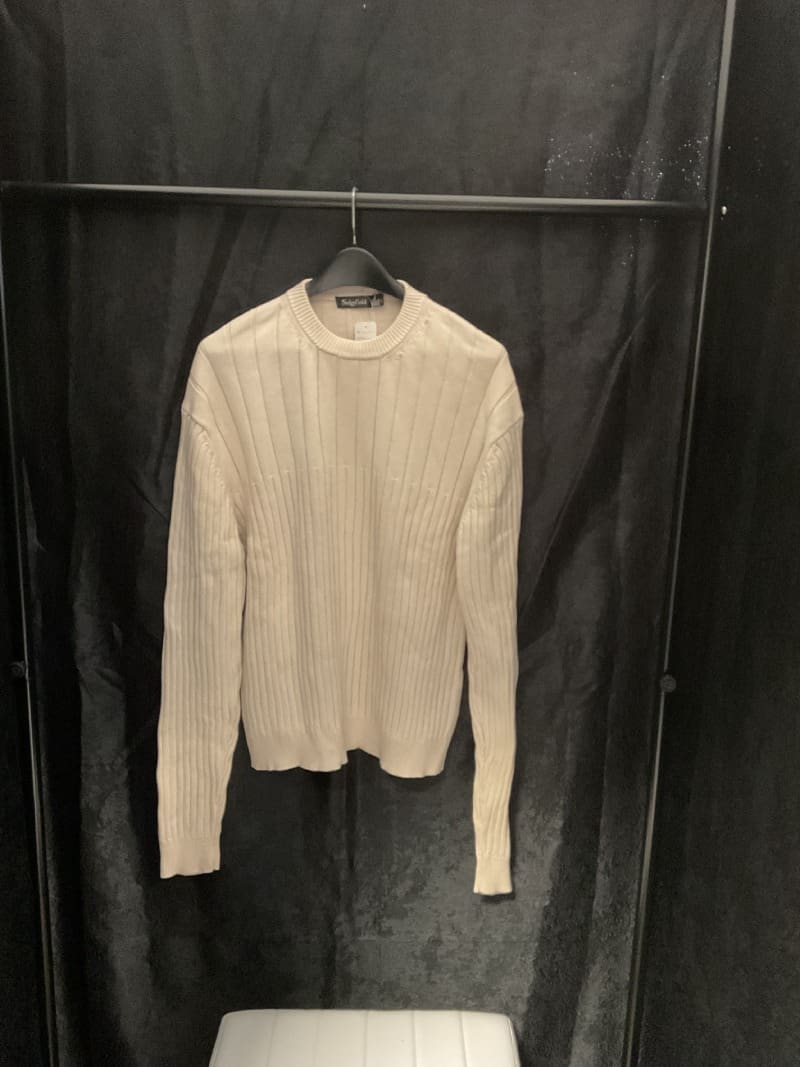 A white sweater hanging on a black wall.