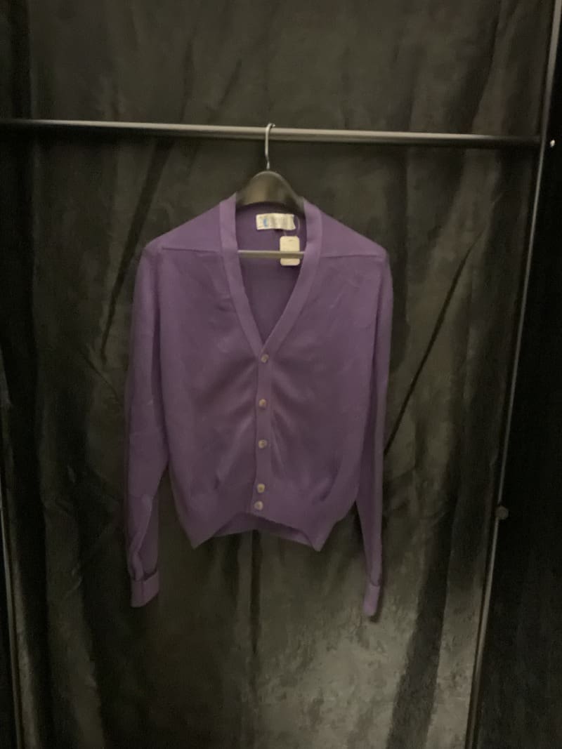 A purple cardigan hanging on a black wall.