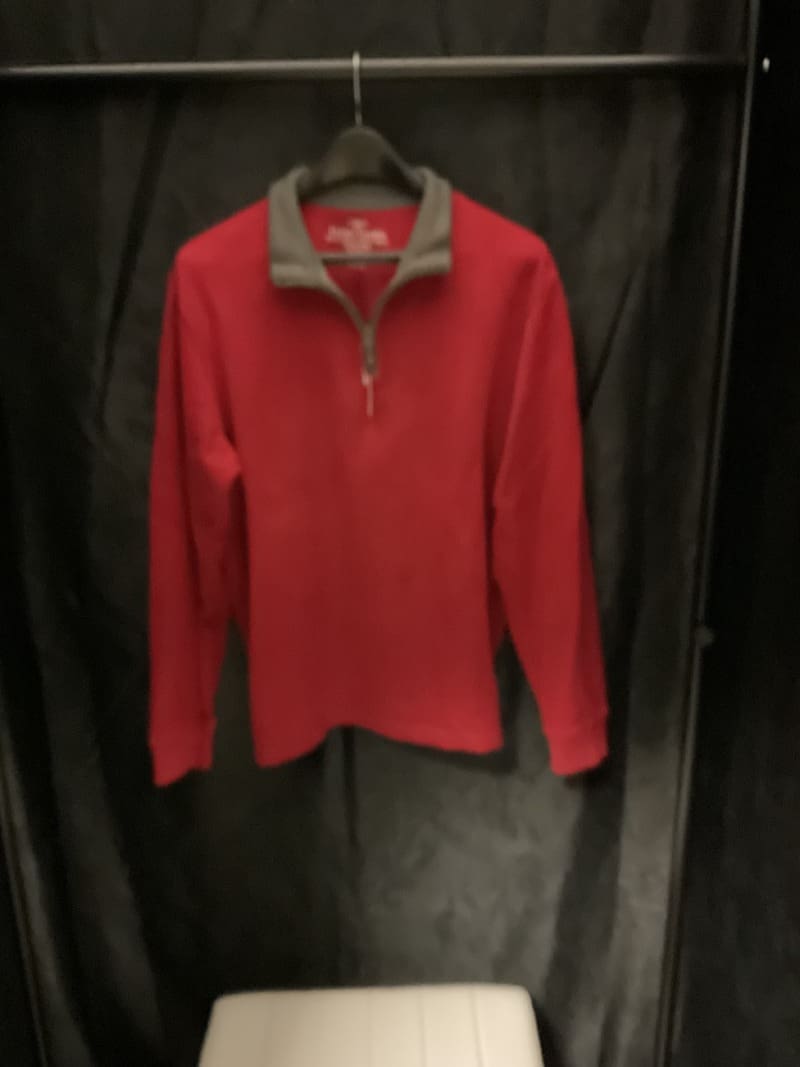 A red and gray jacket hanging on a black wall.