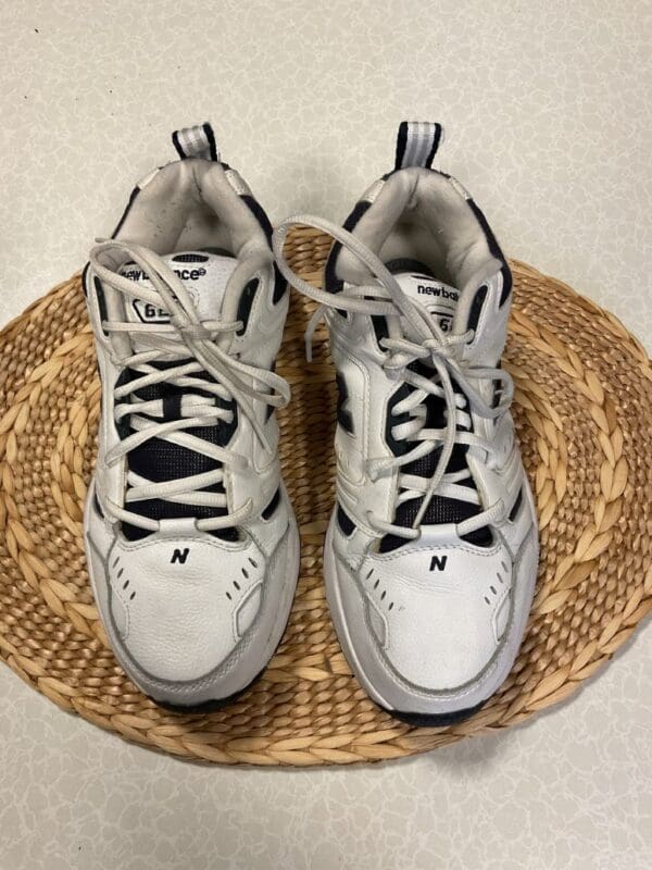 A pair of white and black sneakers sitting on top of a straw mat.