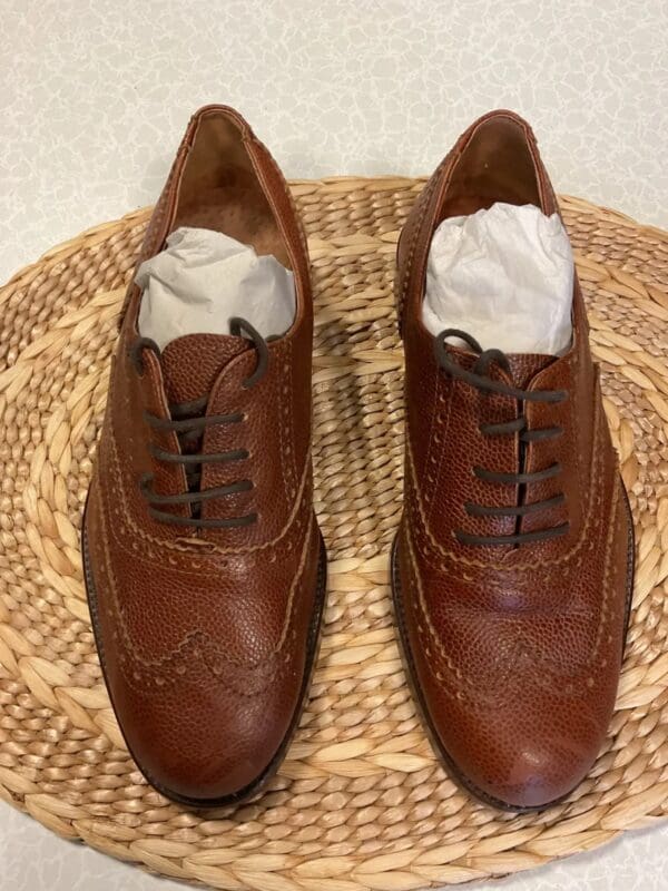 A pair of brown shoes sitting on top of a wicker basket.